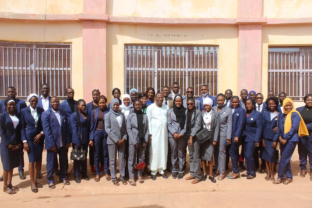 Une quarantaine d’étudiants et de membres du personnel en tenue de cérémonie, réunis pour une photographie de groupe devant la salle multifonctionnelle.